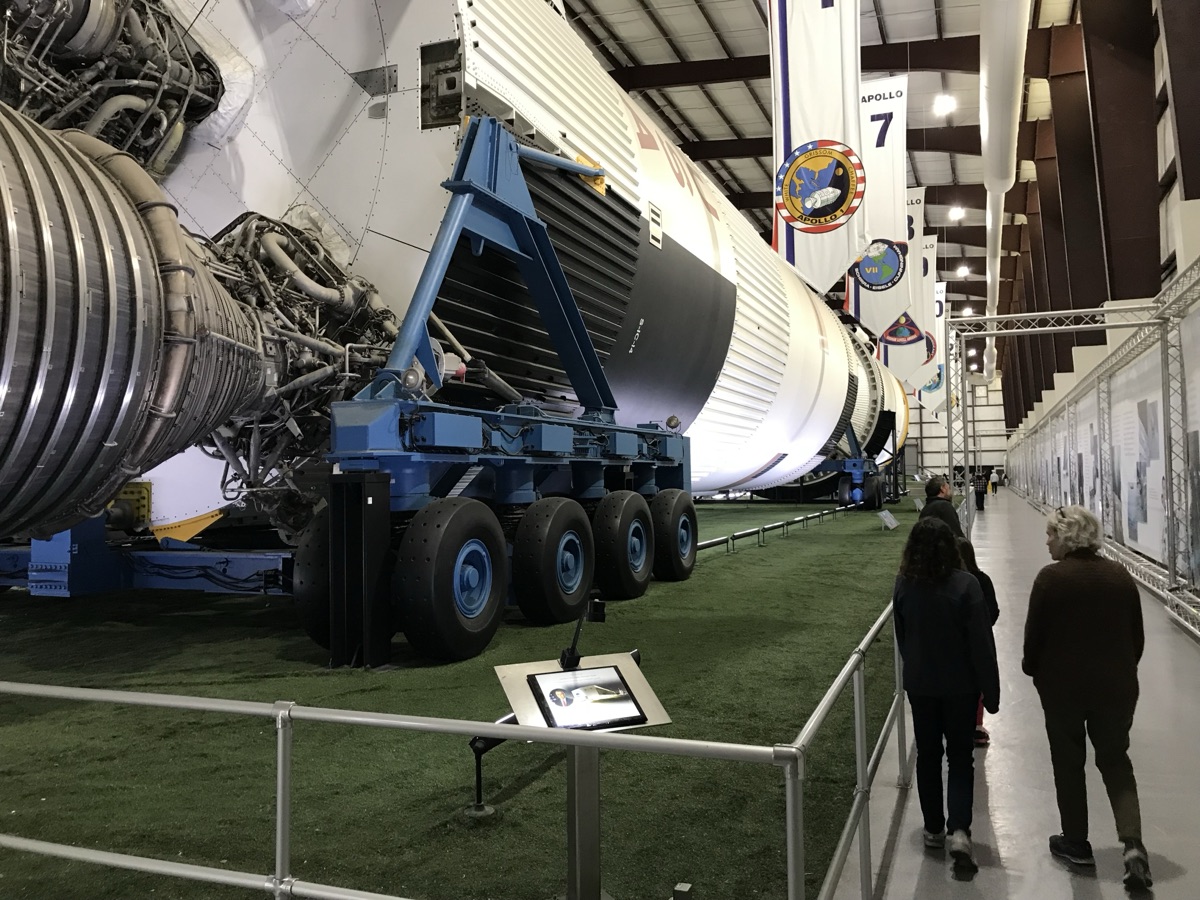 The same Saturn V in 2023 seen from the bottom end, over thirty years later. Now indoors, on artificial turf, with banners hanging above for each of the Apollo missions.